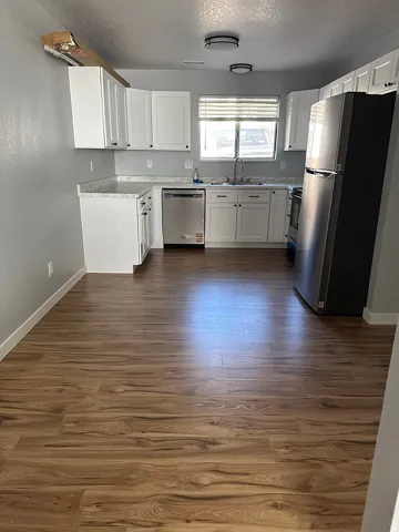 Kitchen featuring white cabinetry, light-toned countertops, stainless steel appliances, and wood-finish flooring