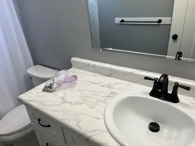 White vanity featuring a white-finish countertop with a drop-in sink, matte black faucet, and a wall-mounted mirror