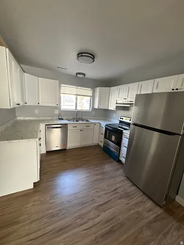 Kitchen featuring wood-finish flooring, white cabinetry with dark hardware, a stainless steel refrigerator, a stainless steel dishwasher, and a stainless steel range