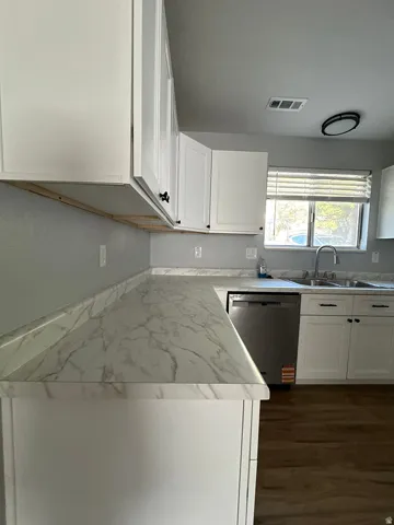 White cabinetry with black hardware, marble-look countertops, stainless steel dishwasher, and wood-finish flooring