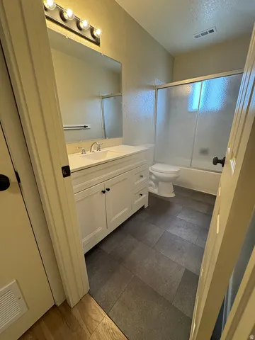 White vanity with integrated sink, chrome faucet, wall-mounted mirror, overhead vanity lighting, and gray tiled flooring