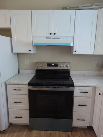 White shaker-style cabinetry with black hardware, stainless steel range, white range hood, light-toned countertops, and wood-finish flooring