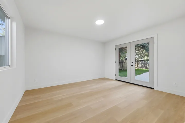 Wood-finish flooring, white painted walls, recessed ceiling lighting, a window, and French doors leading to a private outdoor area