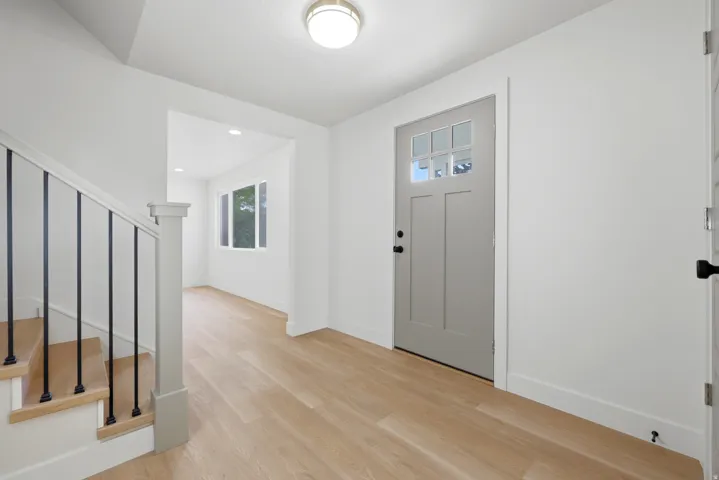 Light wood-finish flooring, staircase with dark metal balusters, and a light gray entry door with glass panels