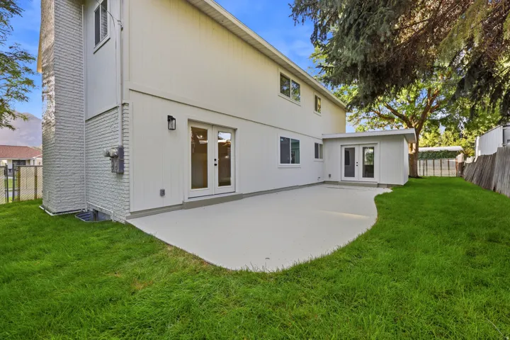 Spacious concrete patio with double French doors, a secondary building with double doors, and a wood privacy fence