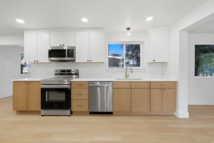 Two-tone cabinetry with white upper and wood-finish lower cabinets, stainless steel appliances, white countertops, and wood-finish flooring