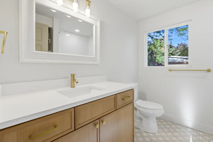 Wood-finish vanity with gold-tone hardware, white countertop, and integrated rectangular sink