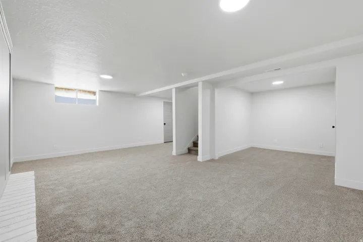 Expansive carpeted area with recessed lighting, a window, and a painted brick fireplace surround