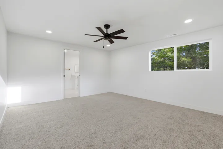 Spacious room featuring neutral carpeting, a modern ceiling fan, recessed lighting, and a large window