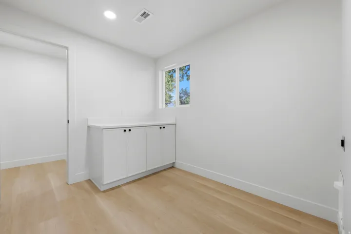 Recessed lighting, wood-finish flooring, built-in cabinetry with dark hardware, a window, and an open doorway