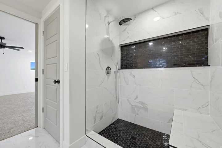 Walk-in shower with clear glass enclosure, white marble-look wall tiling, and black hexagonal floor tiling