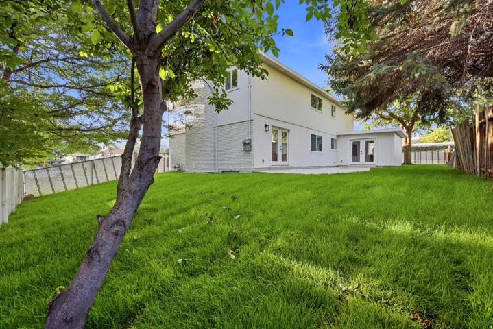 Expansive rear lawn with mature trees, a concrete patio, and multiple exterior doors providing direct outdoor access