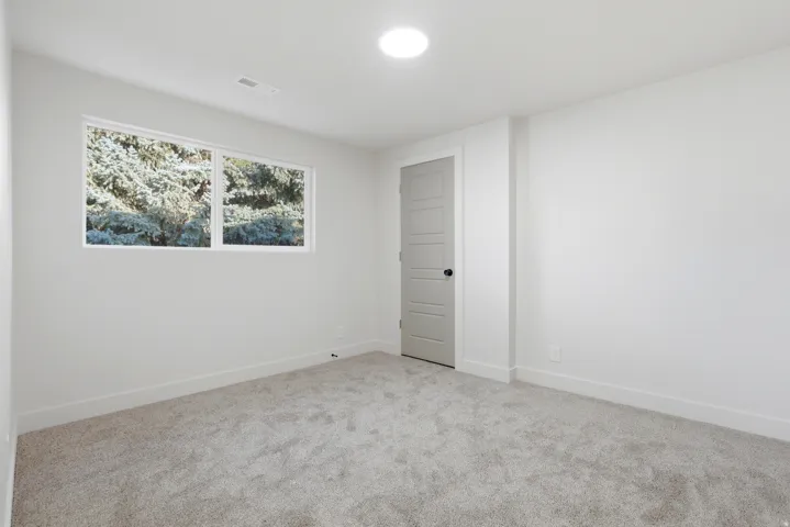 Bright interior with light gray carpeting, a multi-pane window, and a gray paneled door with a black knob