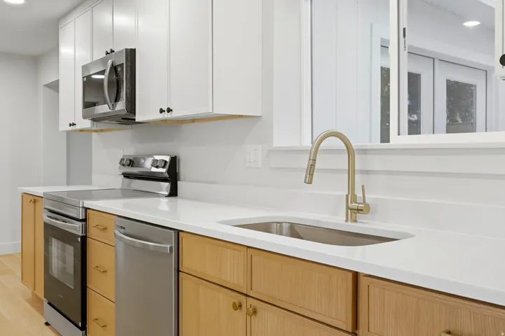 Kitchen featuring two-tone cabinetry, white countertops, stainless steel appliances, and a gold-tone gooseneck faucet