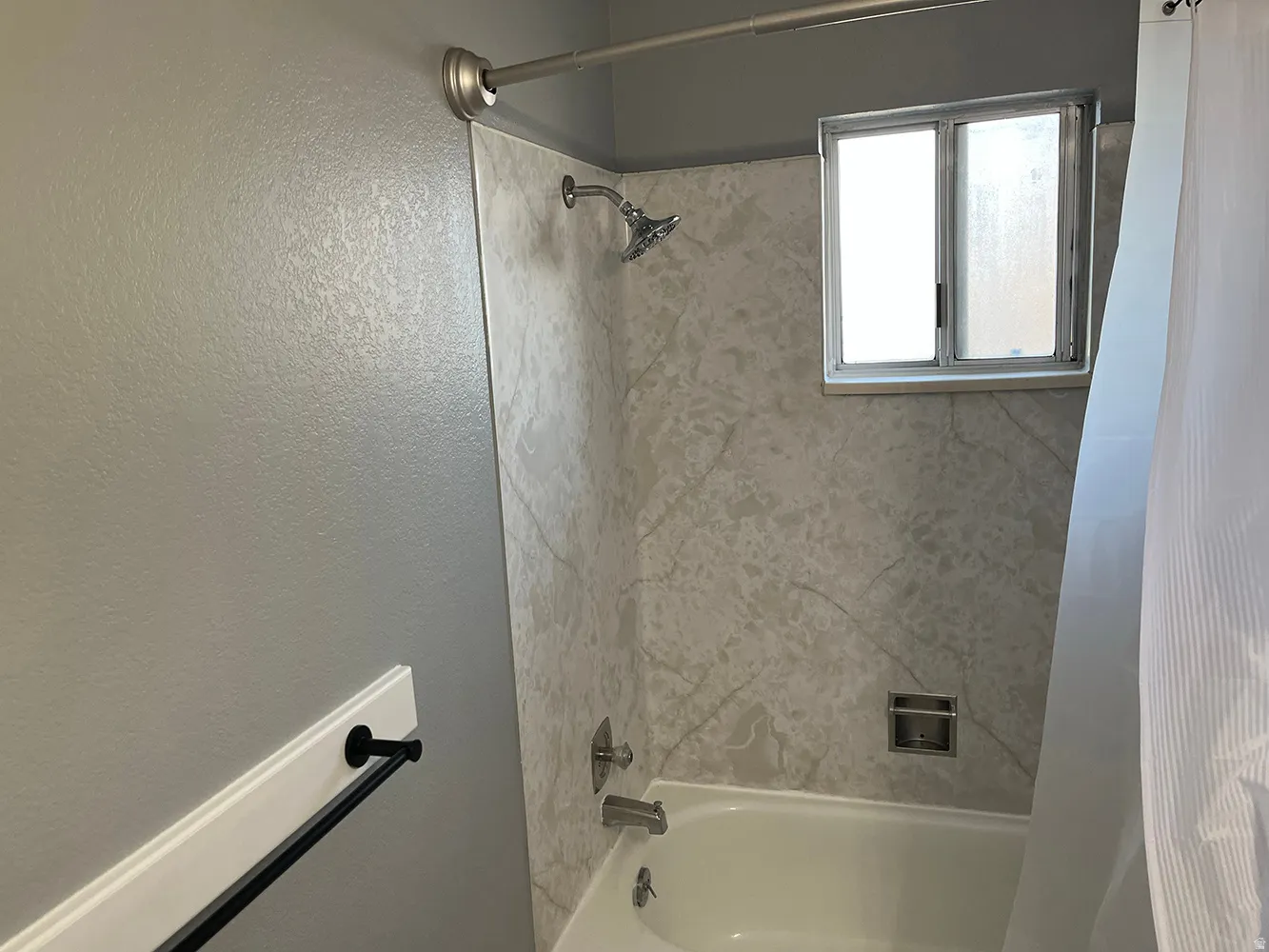 Bathtub with patterned wall surround, integrated shower/tub fixtures, and a frosted glass window
