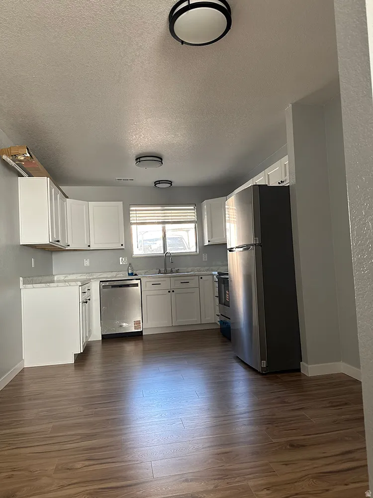 Kitchen featuring white cabinetry, stainless steel appliances, light-toned countertops, wood-finish flooring, and flush-mount lighting fixtures