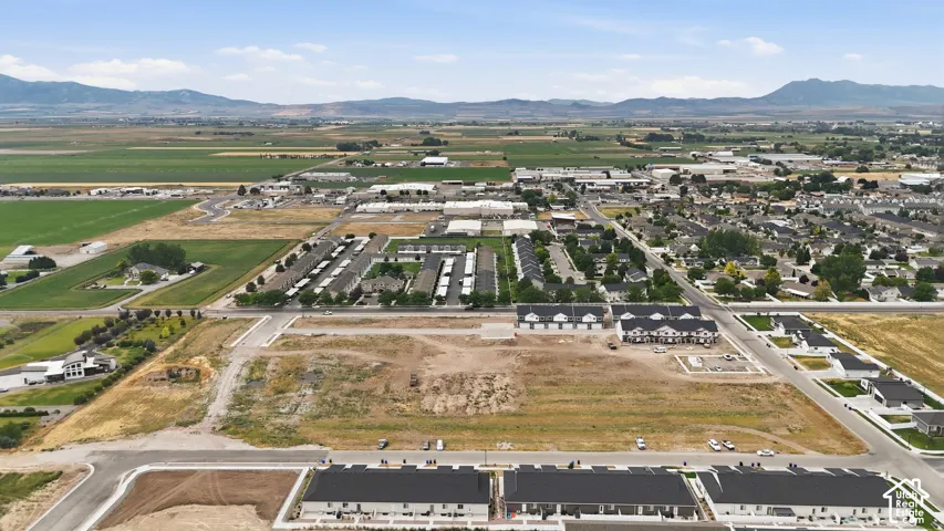 Expansive development site with established infrastructure, surrounded by a mix of residential and agricultural areas, featuring distant mountain backdrops