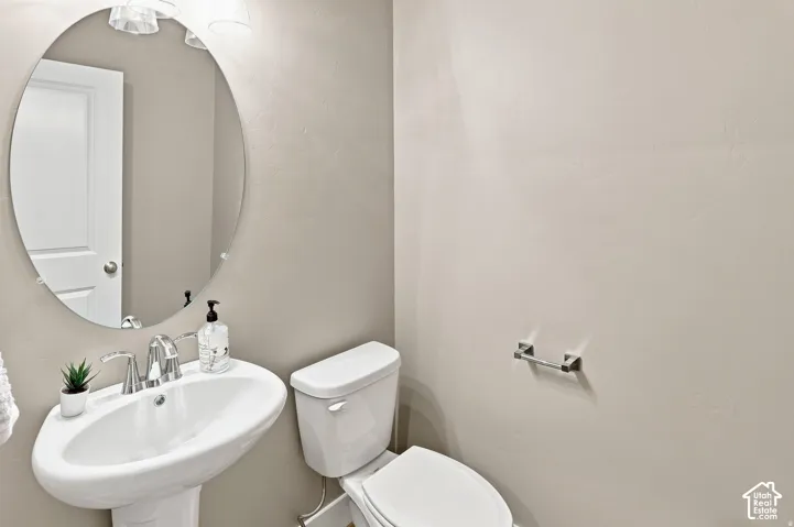 Pedestal sink with chrome faucet, oval mirror, and overhead vanity lighting