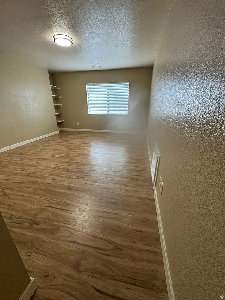 Wood-finish flooring, built-in shelving, window with blinds, and flush-mount ceiling light