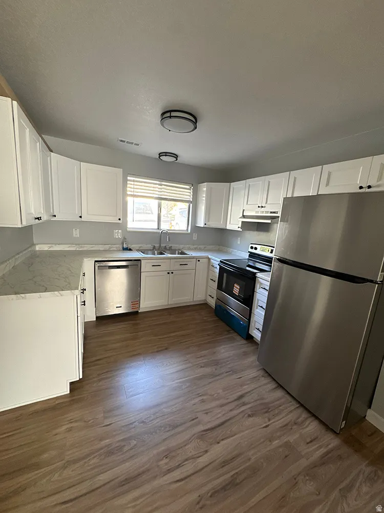 Kitchen featuring wood-finish flooring, white cabinetry with dark hardware, a stainless steel refrigerator, a stainless steel dishwasher, and a stainless steel range