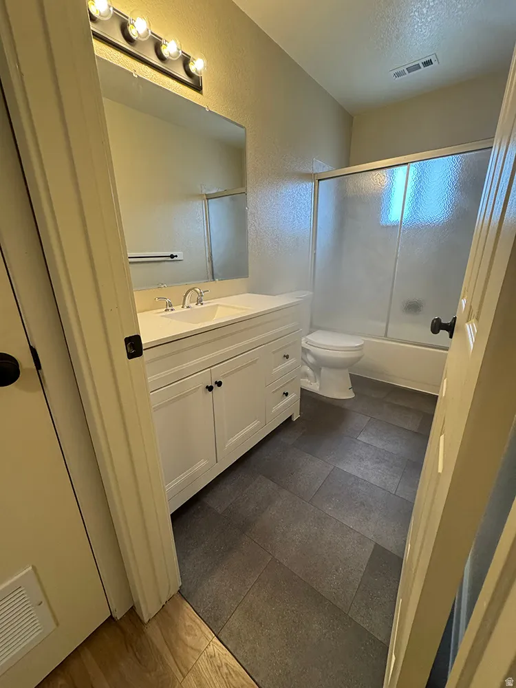 White vanity with integrated sink, chrome faucet, wall-mounted mirror, overhead vanity lighting, and gray tiled flooring