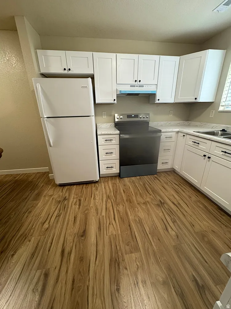 L-shaped kitchen featuring white cabinetry, light-toned countertops, and wood-finish flooring