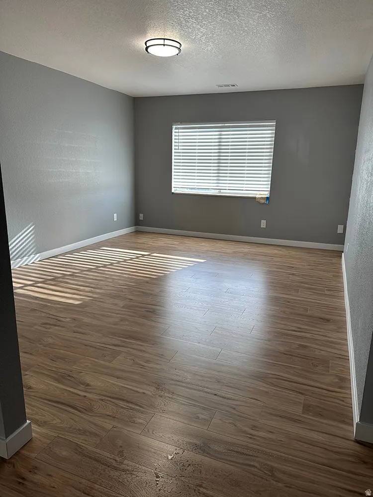 Spacious room featuring wood-finish flooring, a window with blinds, and an overhead flush-mount light fixture