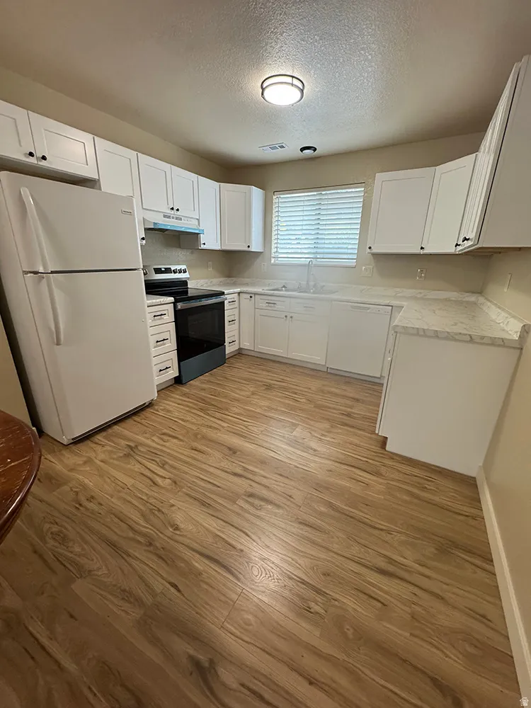 Kitchen featuring white cabinetry with black hardware, white appliances, light-toned countertops, and wood-finish flooring