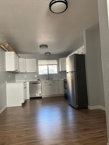 Kitchen featuring wood-finish flooring, white cabinetry, light-toned countertops, stainless steel appliances, and flush-mount ceiling lighting