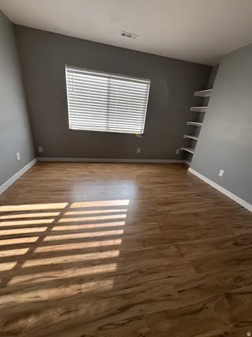 Wood-finish flooring, built-in shelving, white baseboards, and window blinds