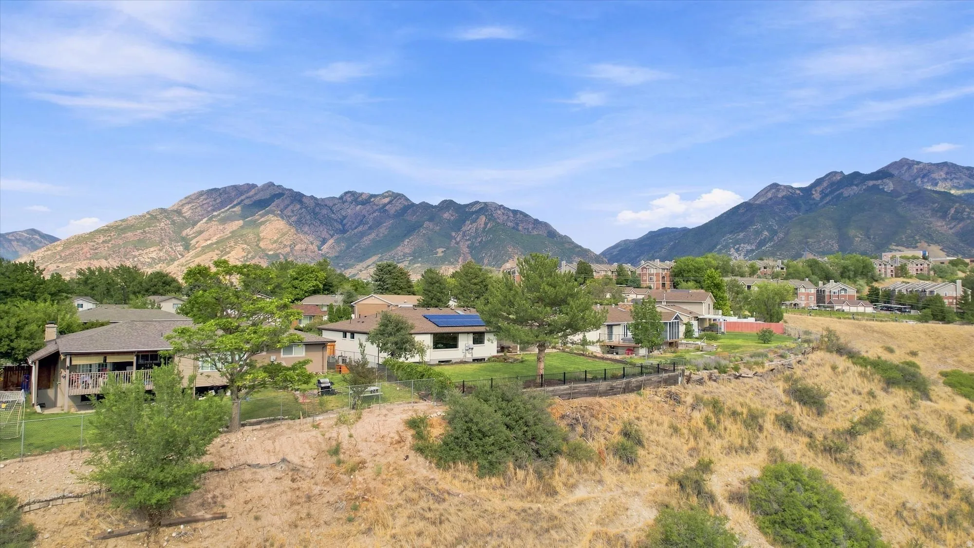 Mountain backdrop, residential area, mature trees, solar panels, sloped terrain