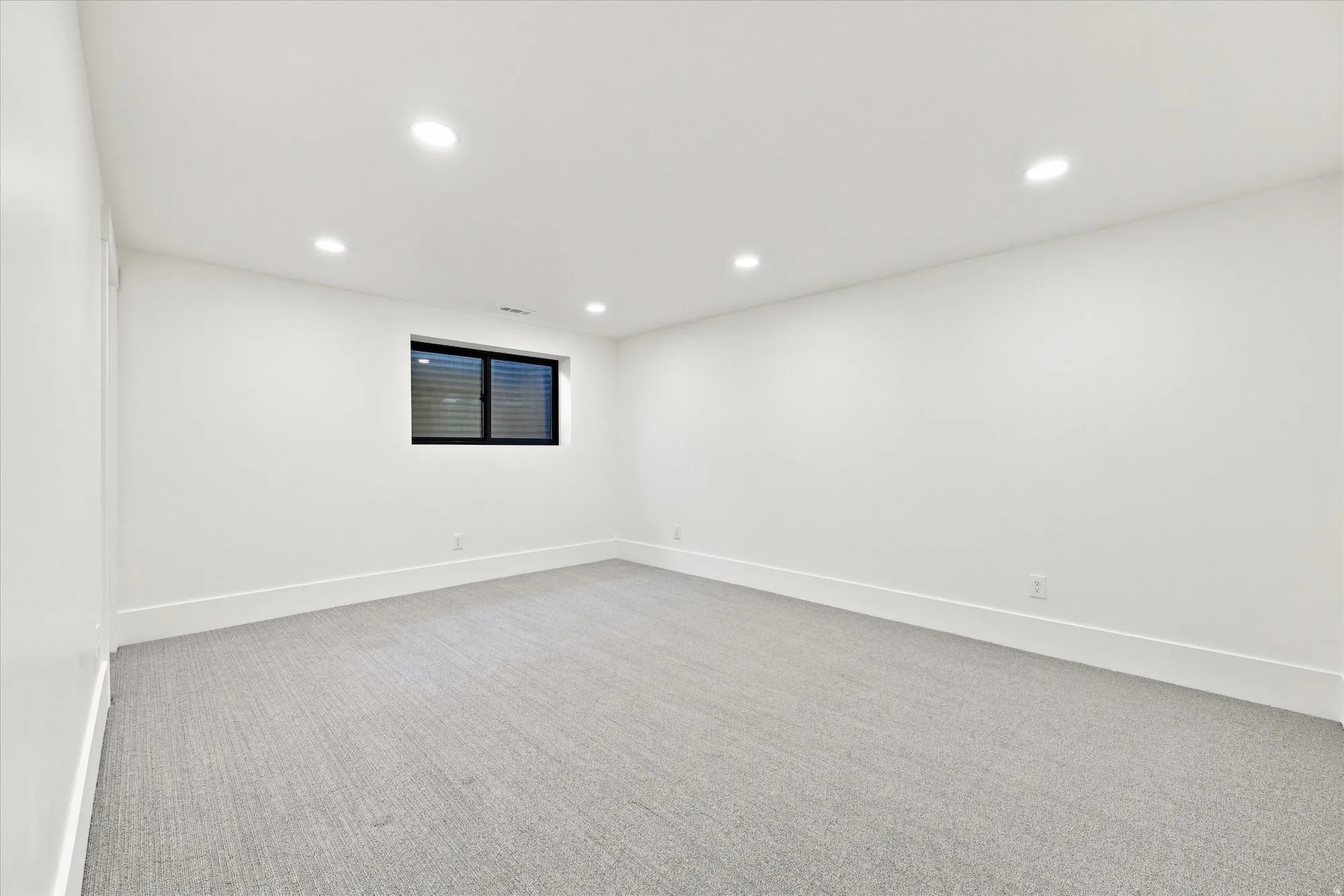 Recessed lighting, soft gray carpet, white painted walls, and a black-framed window