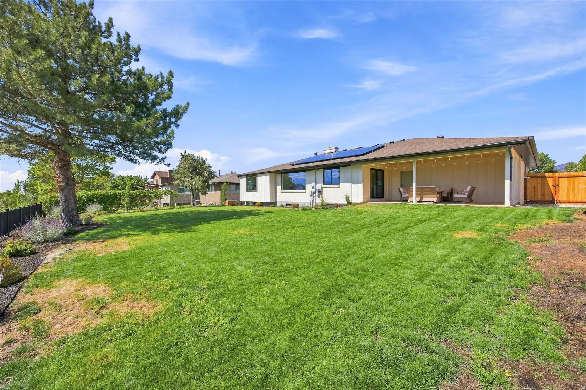 Expansive grassy backyard featuring a large patio cover, solar panels, and a wood privacy fence