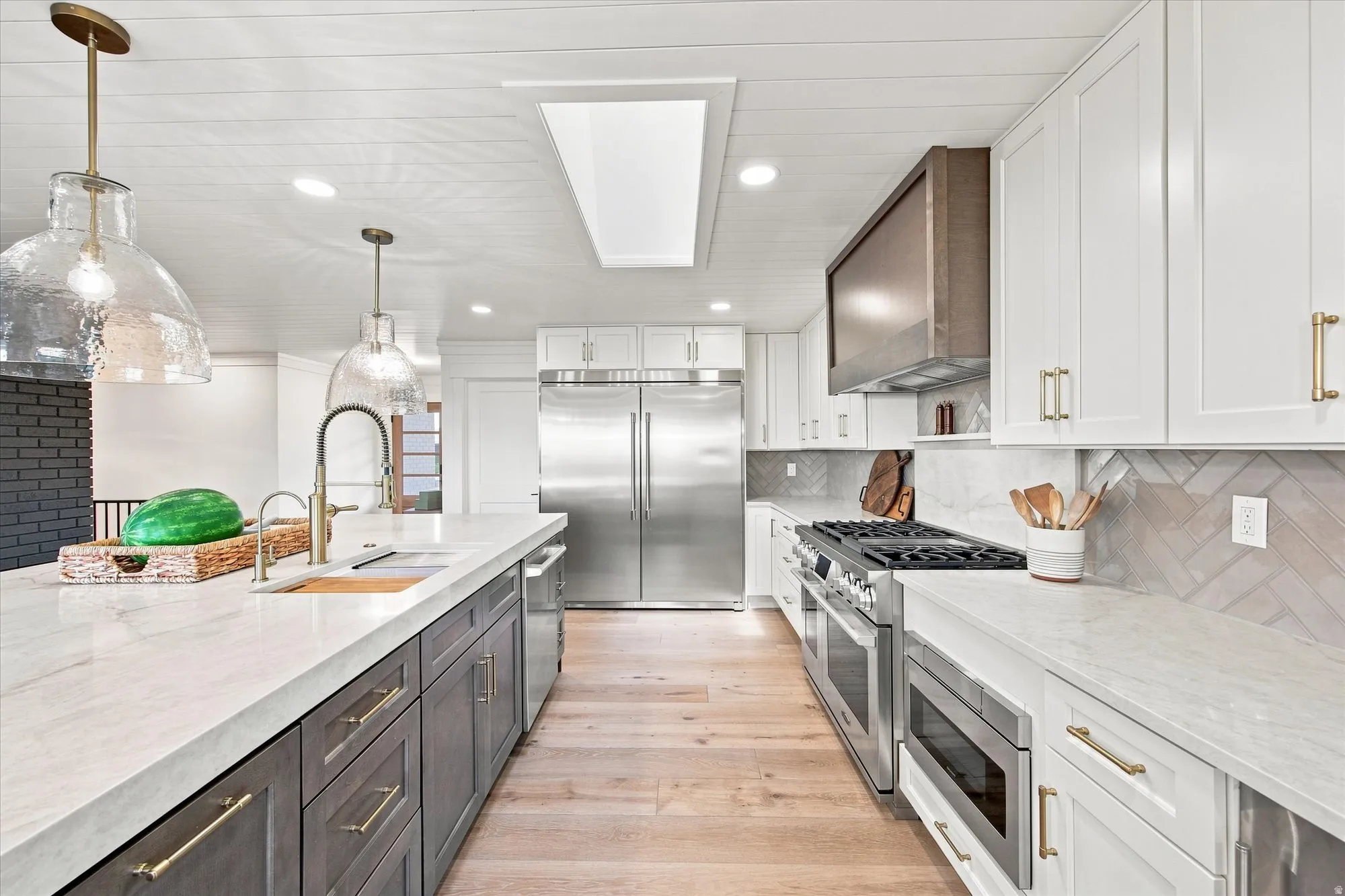 Kitchen featuring white and gray cabinetry, light wood-finish flooring, stainless steel appliances, and a herringbone tile backsplash