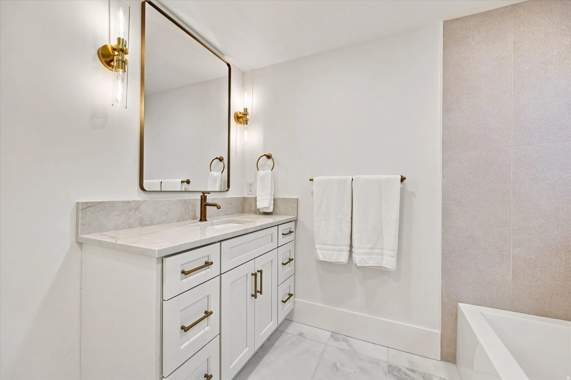 White vanity with bronze hardware, a light-toned countertop, and an integrated rectangular sink