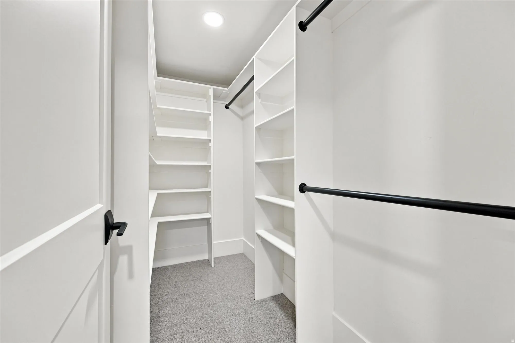 Walk-in closet with built-in shelving, black hanging rods, and recessed lighting