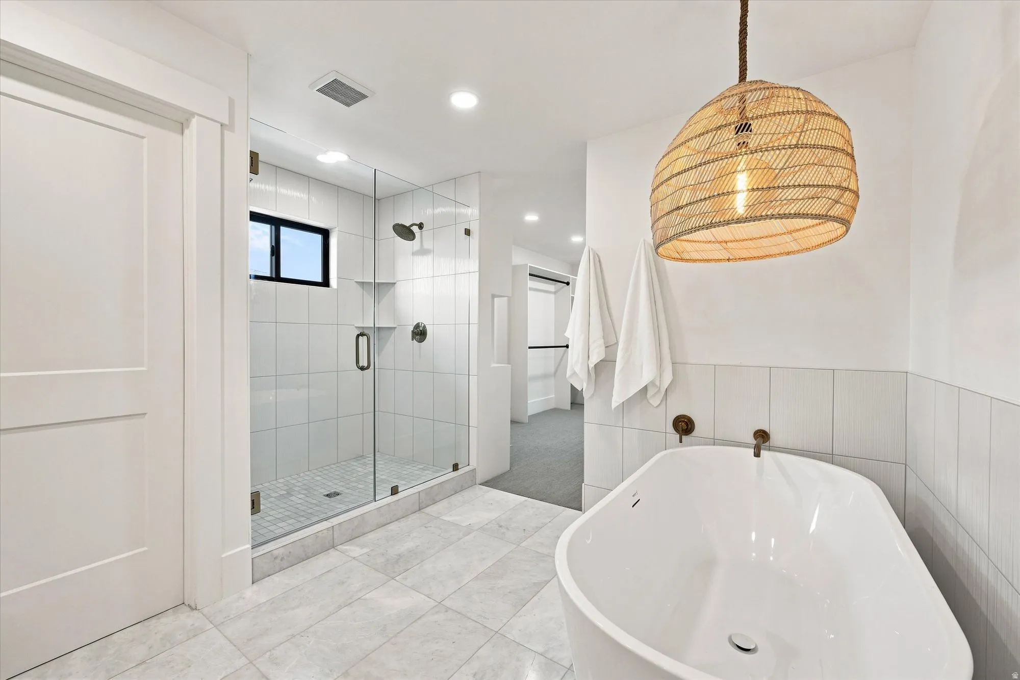 Freestanding soaking tub, glass-enclosed shower, tiled flooring, integrated wall shelving, and a woven pendant light fixture