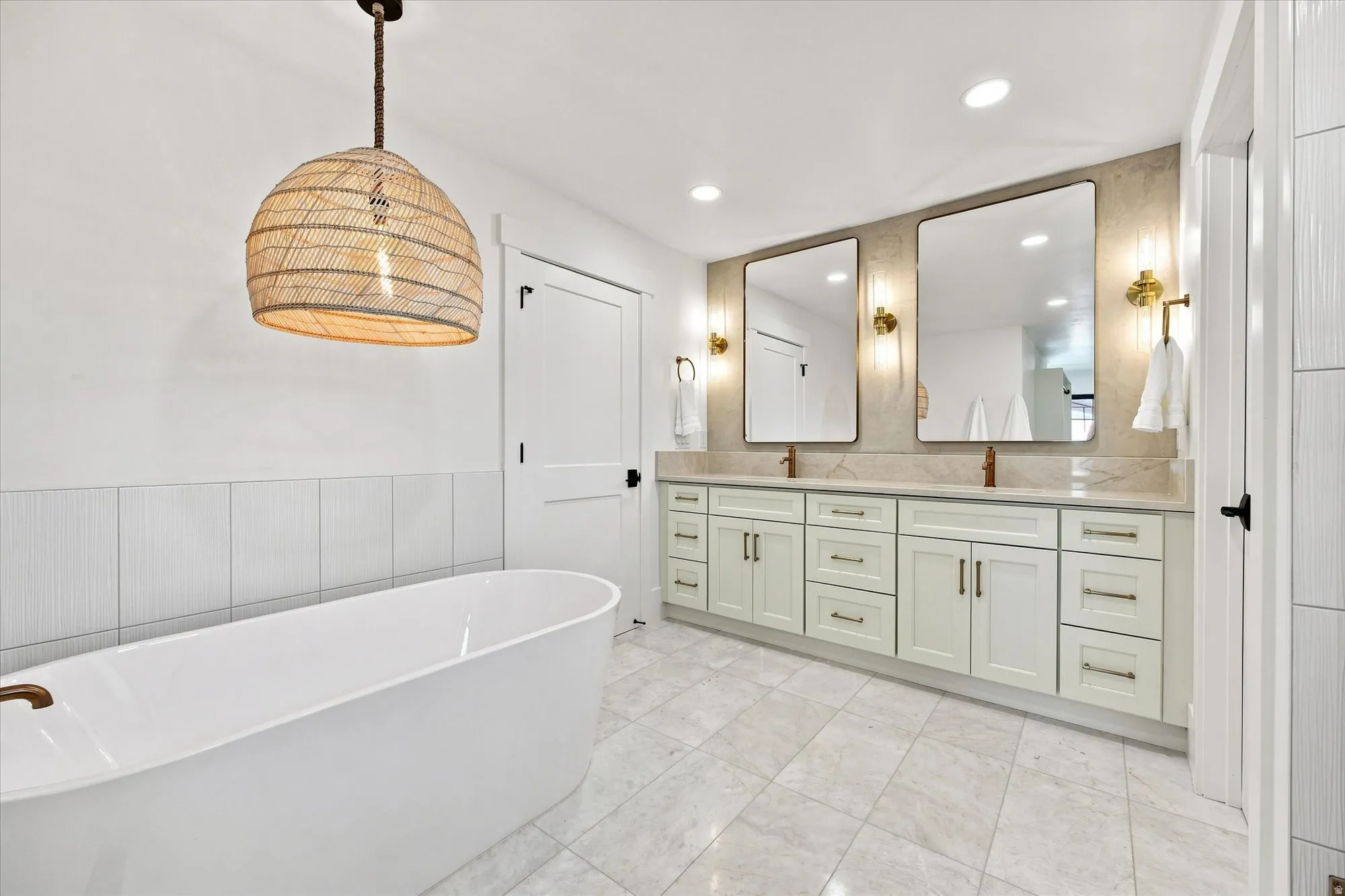 Freestanding soaking tub with a bronze-finish faucet, dual vanity with light-colored cabinetry, stone-finish countertop, and two rectangular wall-mounted mirrors