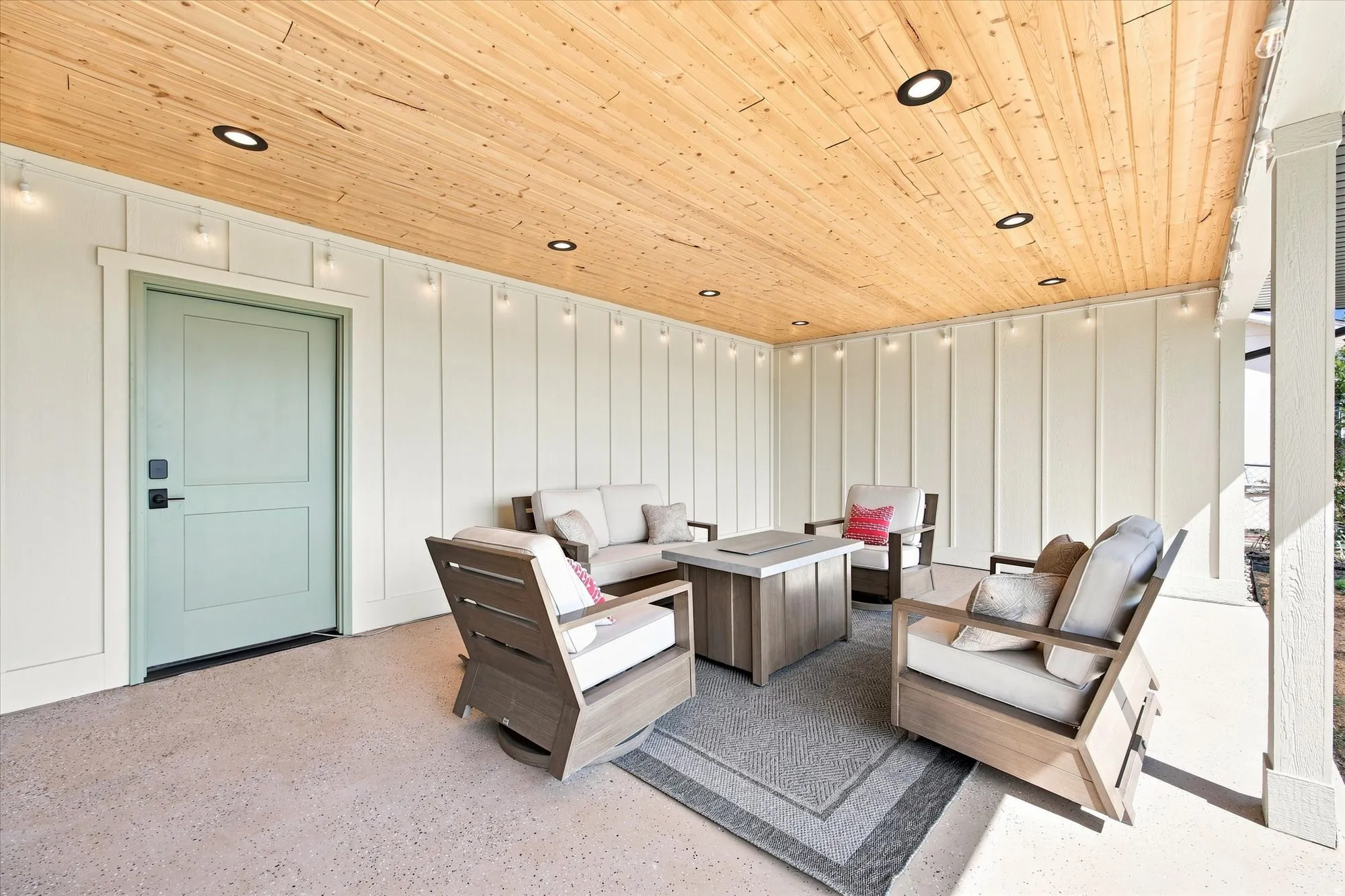 Covered patio featuring a wood-panel ceiling with recessed lighting, board and batten siding, and an opaque entry door