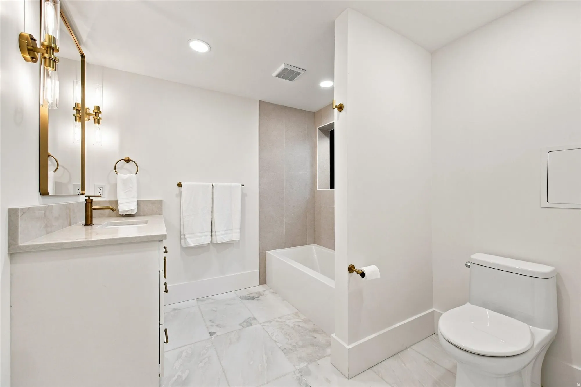 White vanity with a stone countertop, an undermount sink, and a wall-mounted mirror