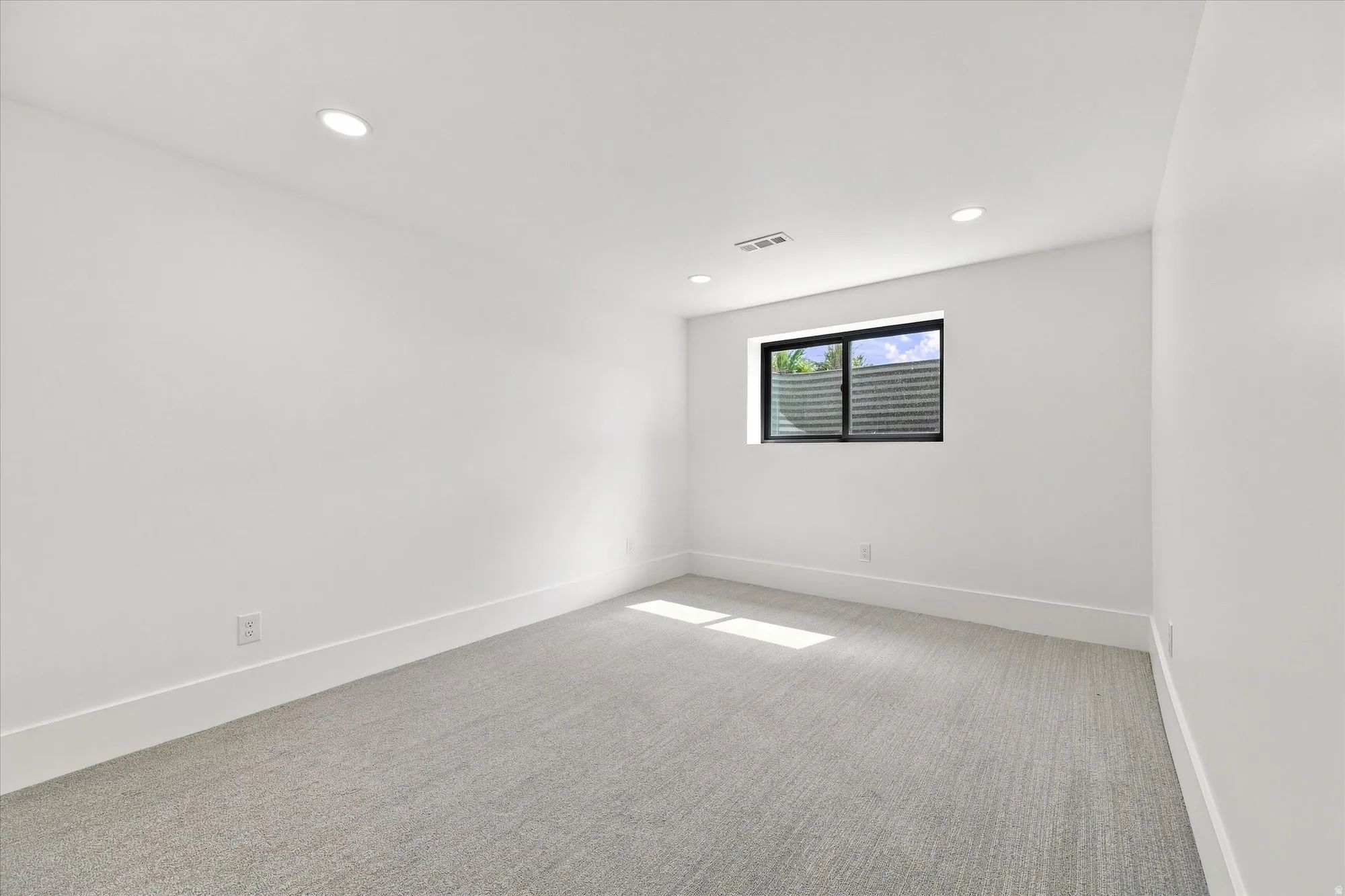 Recessed lighting, light gray carpeting, crisp white walls, and a black-framed window