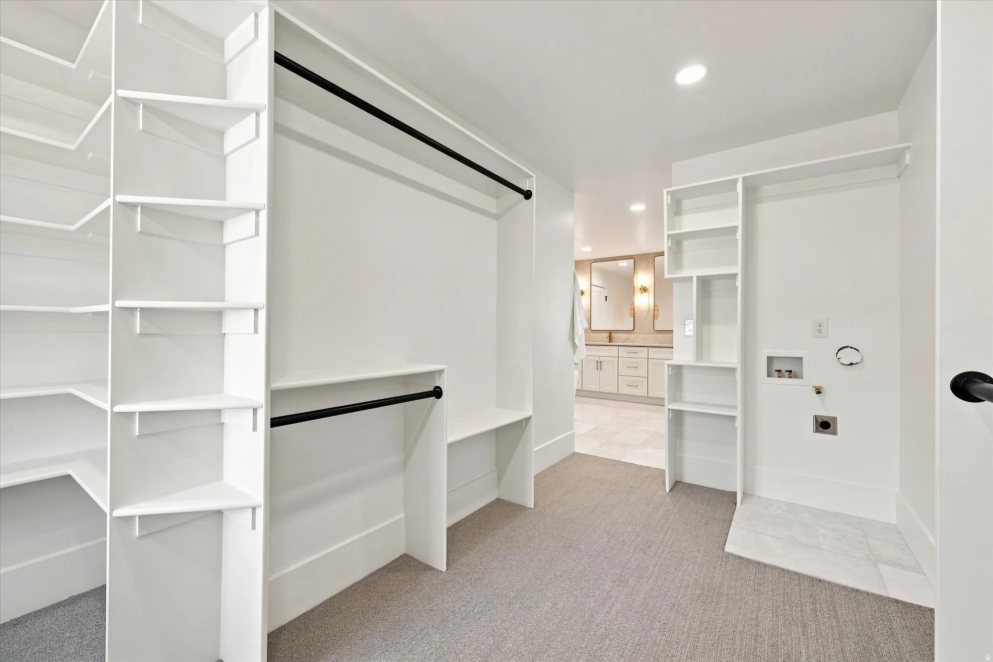 Built-in shelving, black hanging rods, recessed lighting, and laundry hookups with a tiled floor section