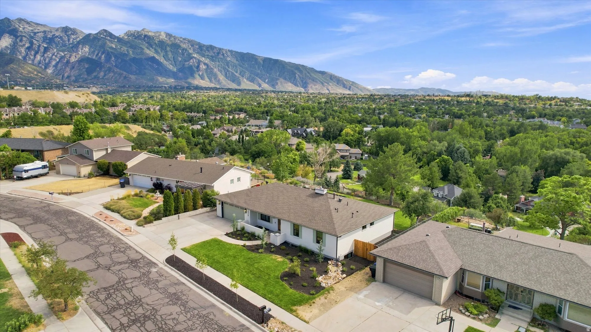 Mountain backdrop, expansive green landscape, paved street, mature trees, residential neighborhood
