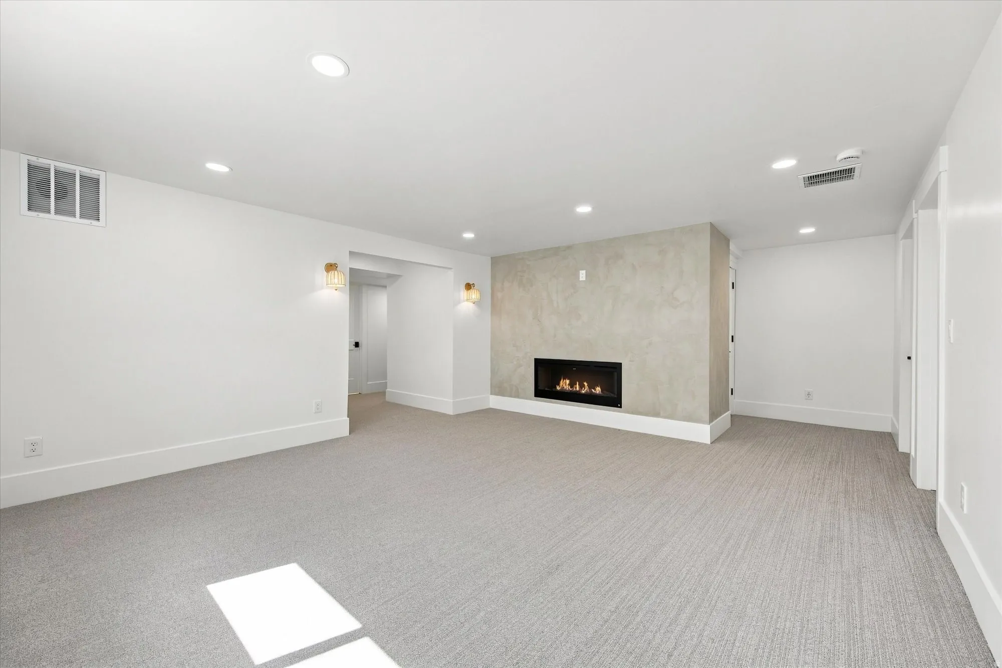 Recessed lighting, wall sconces, modern fireplace with a textured surround, light-toned carpeting, and crisp white trim