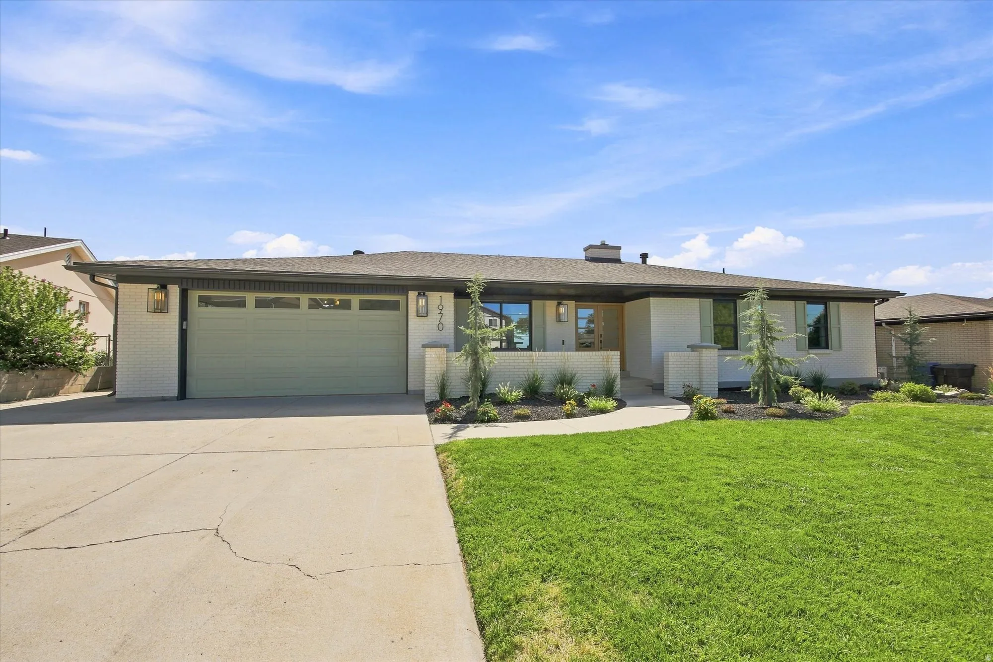 Single-story residence featuring a two-car garage, manicured lawn, curved concrete walkway, and decorative exterior lighting