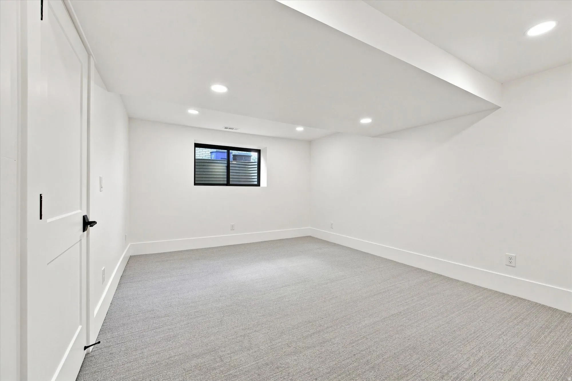 Recessed lighting, light gray carpeting, white walls, white trim, and a window with black trim