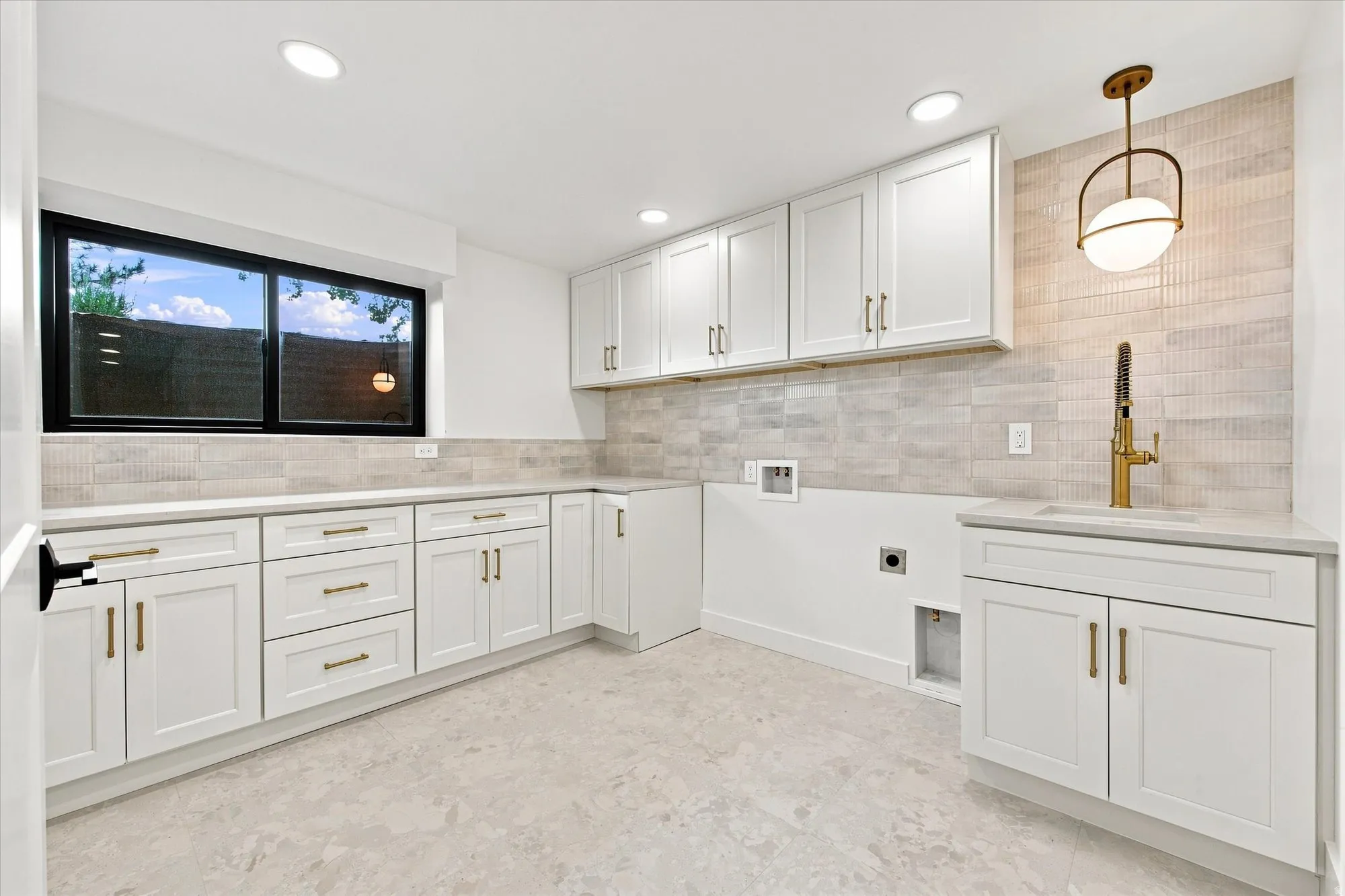 White cabinetry, light-toned countertop, tile backsplash, undermount sink with brass faucet, and recessed lighting