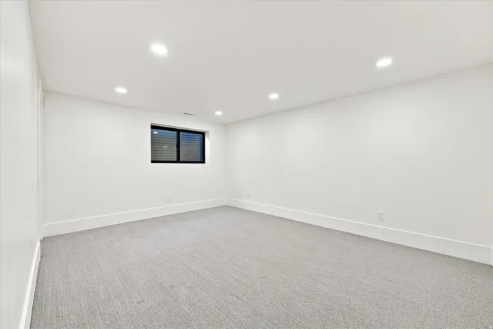 Recessed lighting, soft gray carpet, white painted walls, and a black-framed window