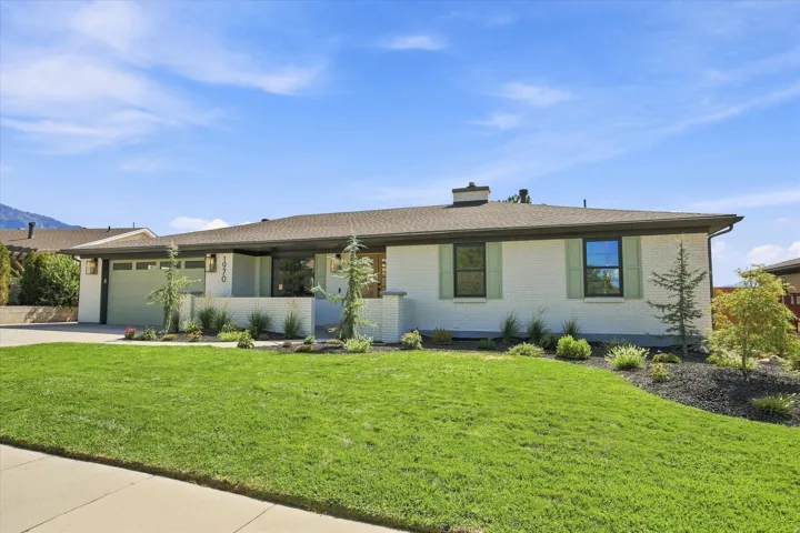 White brick exterior with a dark shingle roof, green garage door, and light green window shutters