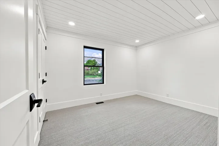 White paneled ceiling with recessed lighting, single window with black trim, gray patterned carpet, and white paneled doors with matte black hardware